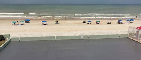 En vy över stranden från en balkong, med en klar himmel, en sandstrand och flera parasoller.
