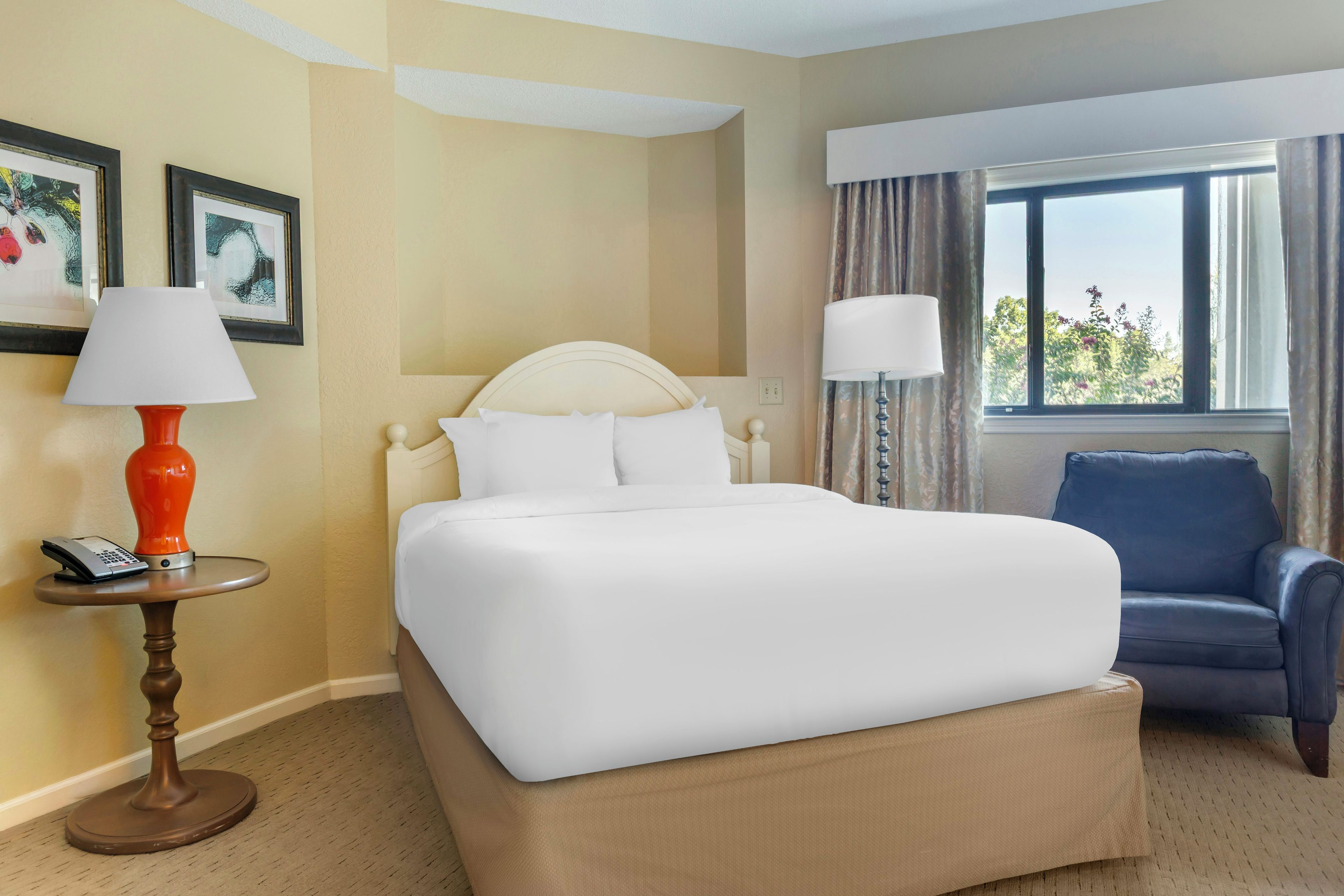 Habitación de hotel con cama, una silla, lámpara, teléfono y ventana con cortinas.