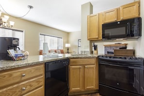 A kitchen with wooden cabinets, a black microwave, a stove, and a coffee maker. - Laurel Crest (Pigeon Forge)