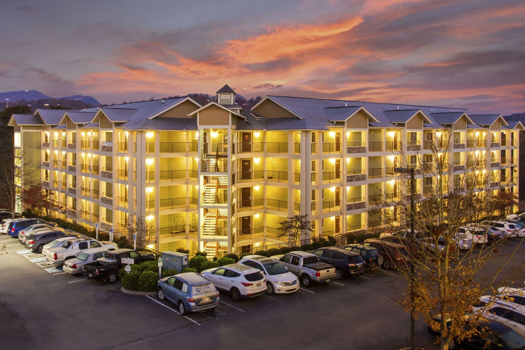 A multi-story hotel with a central staircase, balconies, and a parking lot.