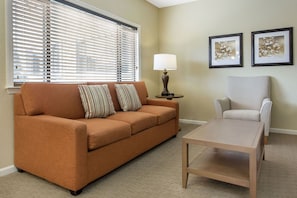 A living room with a sofa, armchair, coffee table, lamp, and two framed pictures on the wall. - Laurel Crest (Pigeon Forge)