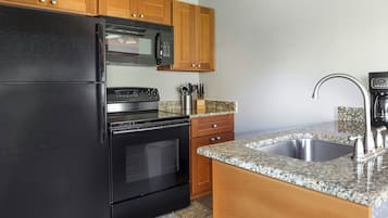 Eine Küche mit einem schwarzen Kühlschrank, einer Mikrowelle, einem Backofen, Holzschränken, einer Granitarbeitsplatte und einem Edelstahl-Spülbecken.