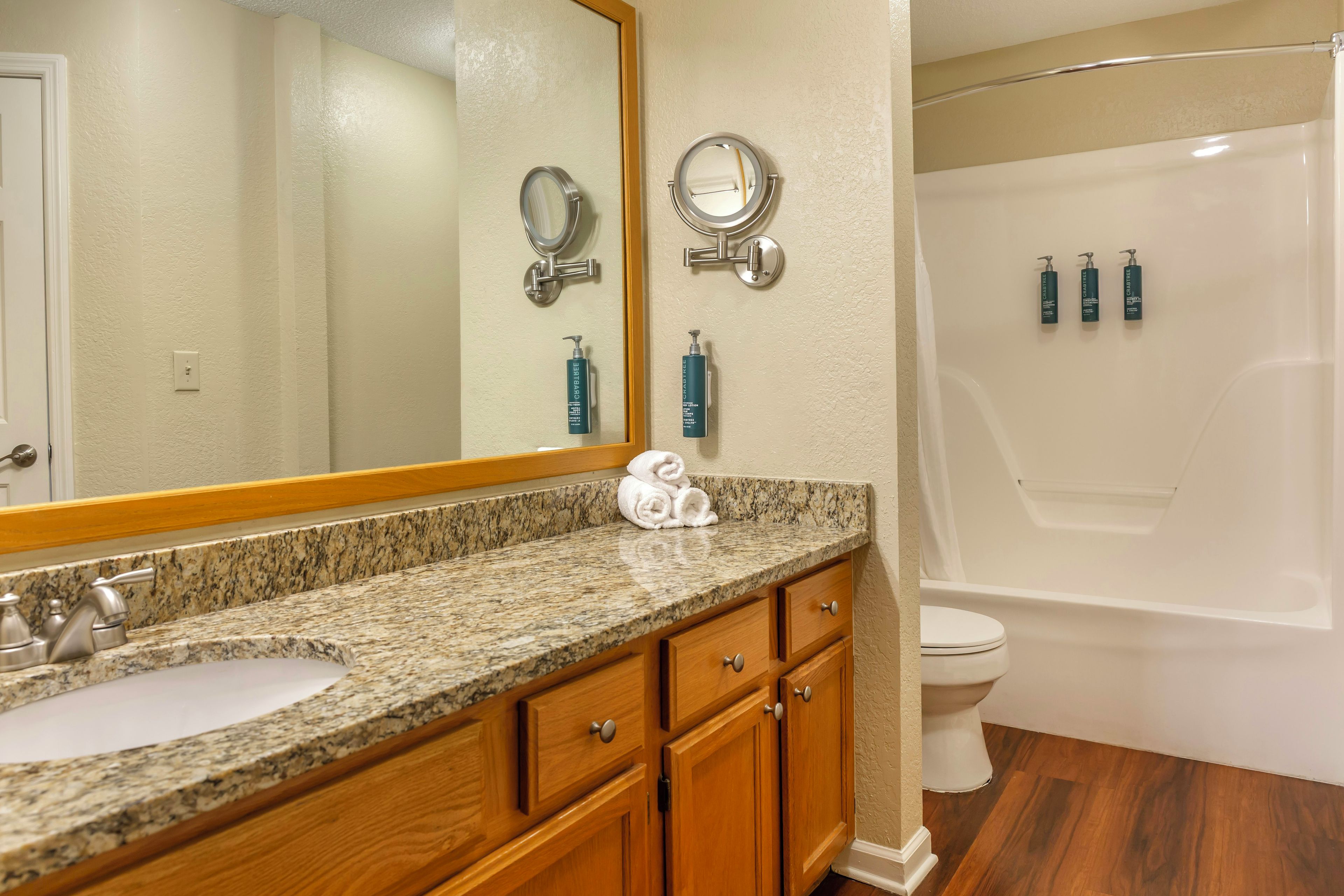 Une salle de bain avec un comptoir en granit, des meubles en bois, un grand miroir, des toilettes et une douche.