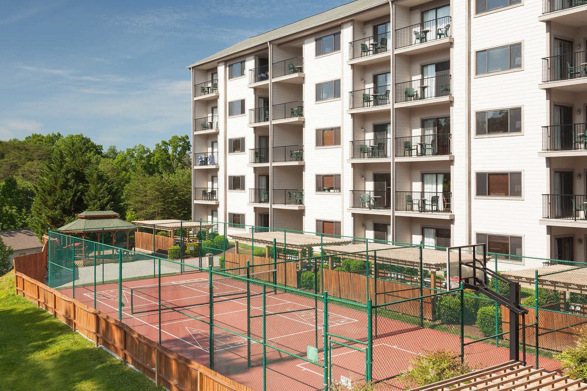 Un edificio residencial de varios pisos con balcones, una cancha de tenis y un pabellón.