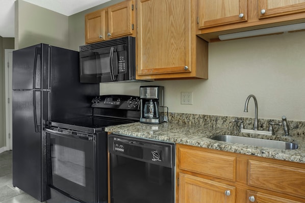 A kitchen with a black refrigerator, a microwave, a stove, a coffee maker, and a sink.