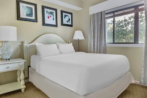 A hotel room with a large bed, two bedside tables, a window with curtains, and three framed pictures on the wall.