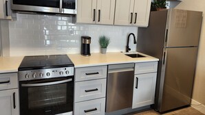 A modern kitchen with stainless steel appliances, white cabinetry, and a tiled backsplash.