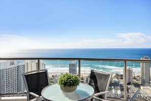 A balcony with a glass table, two chairs, and a potted plant. - Chevron Renaissance Ocean View (Surfers Paradise)