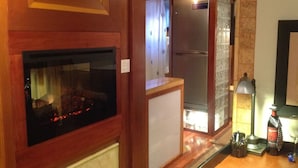 Una habitación acogedora con chimenea, un refrigerador y una lámpara sobre la encimera.