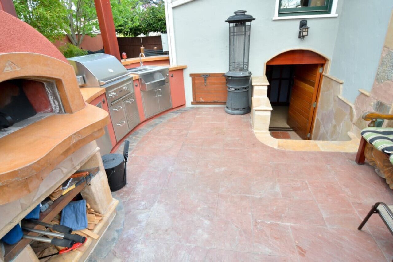 Een terras buiten met een barbecue, een houtkachel en een lantaarn.