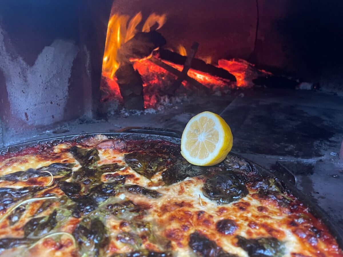 A pizza with a slice of lemon on top, in front of a wood-fired oven.
