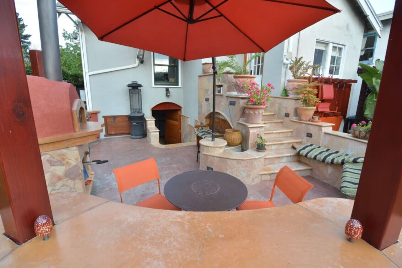 Un espace patio aménagé avec une table et des chaises, entouré de plantes en pot et agrémenté d’une cheminée en pierre.