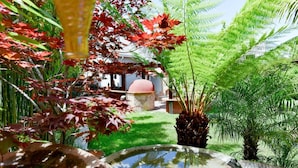 Un jardín con fuente de agua, follaje rojo y una estructura de piedra al fondo.