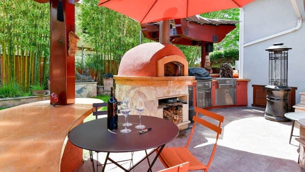 Un patio al aire libre con una mesa de piedra, sillas y un paraguas rojo.