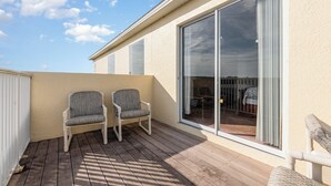 Ein Balkon mit zwei Stühlen, einem Holzboden und einer Schiebetür zu einem Außenbereich.