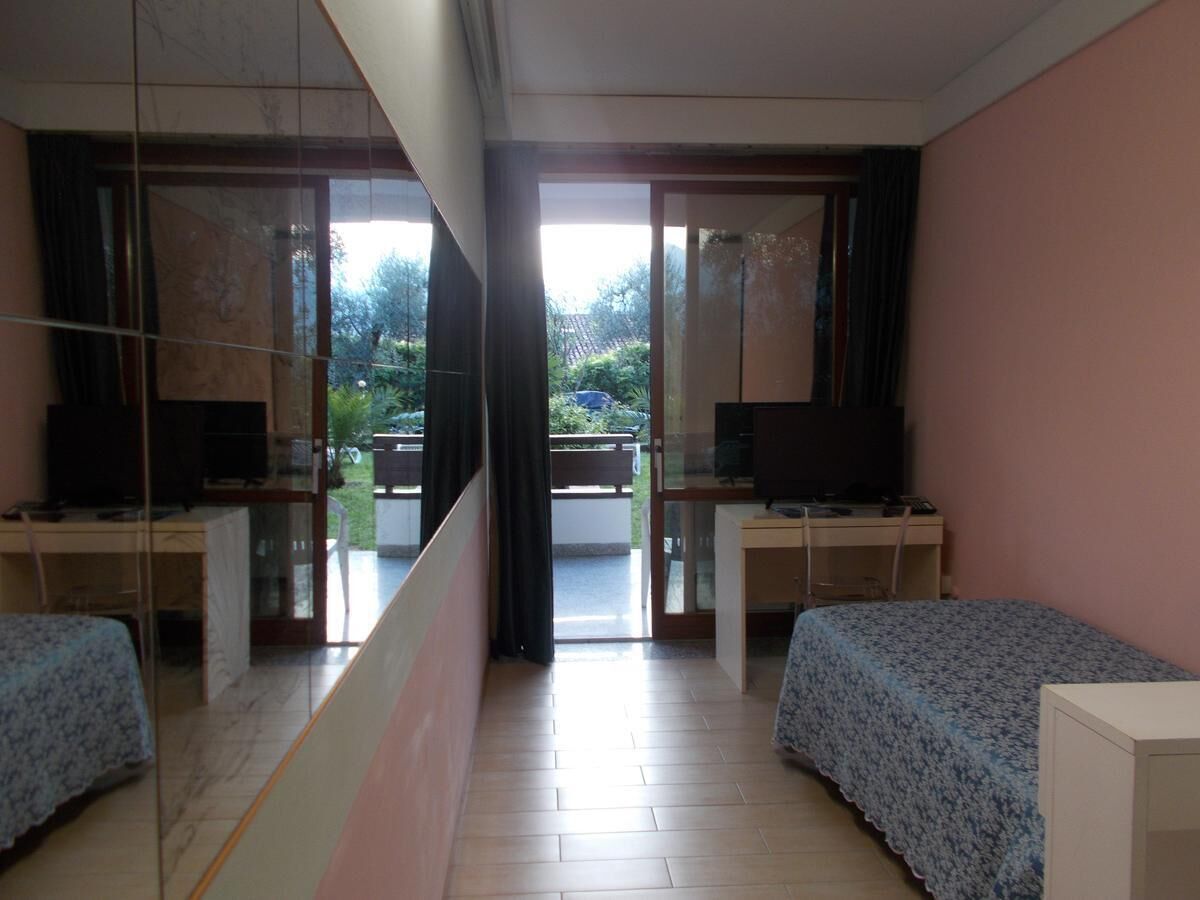 A hotel room with two beds, a desk, a television, and a sliding glass door leading to an outdoor area.