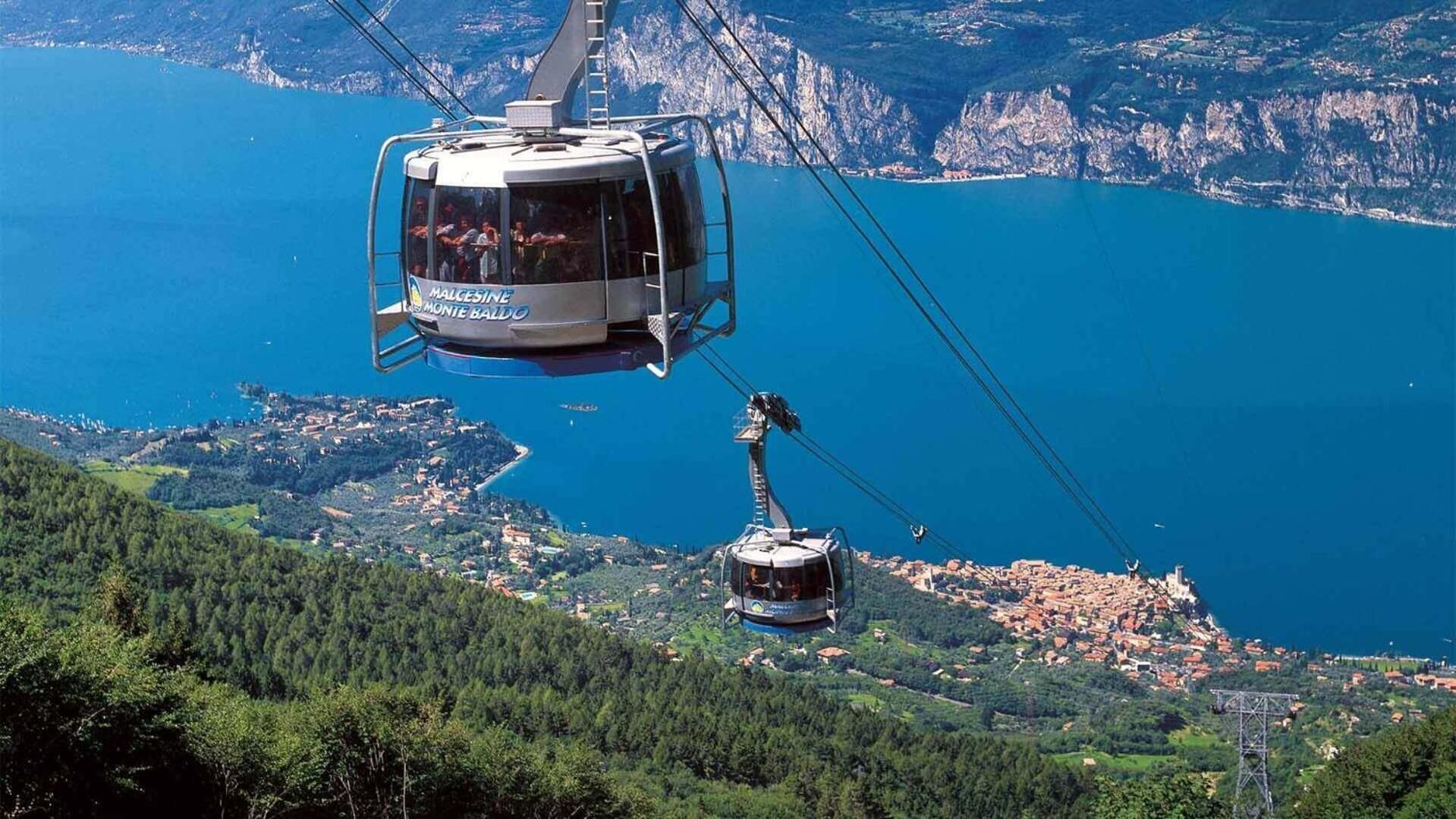A cable car system with cabins suspended by cables over a mountainous landscape and a body of water.