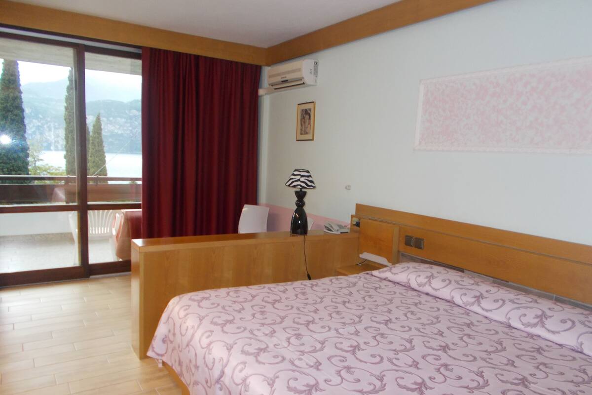 Une chambre d’hôtel équipée d’un lit, d’un bureau, d’une chaise, d’une fenêtre donnant sur un paysage agréable et d’un appareil de climatisation.