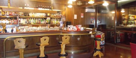 A bar area with a wooden counter, multiple shelves of bottles, and four stools.