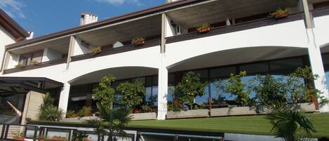 Un edificio moderno con techo plano, varios balcones con plantas en macetas y un césped bien cuidado.