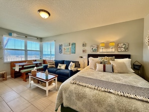 A cozy bedroom with a bed, a sofa, a dining table, and a bench.
