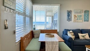 A cozy room with a wooden bench, a table with a woven placemat, a blue sofa, and a view of the sea through large windows. - The Sea Star is an adorable seaside studio with a gorgeous ocean view! (Daytona Beach)