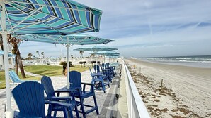 A beachside seating area with blue Adirondack chairs and striped umbrellas, overlooking the ocean. - The Sea Star is an adorable seaside studio with a gorgeous ocean view! (Daytona Beach)