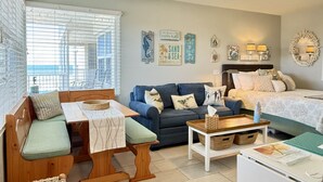 A cozy living room with a sofa, a small table, a bench, and a bed. - The Sea Star is an adorable seaside studio with a gorgeous ocean view! (Daytona Beach)