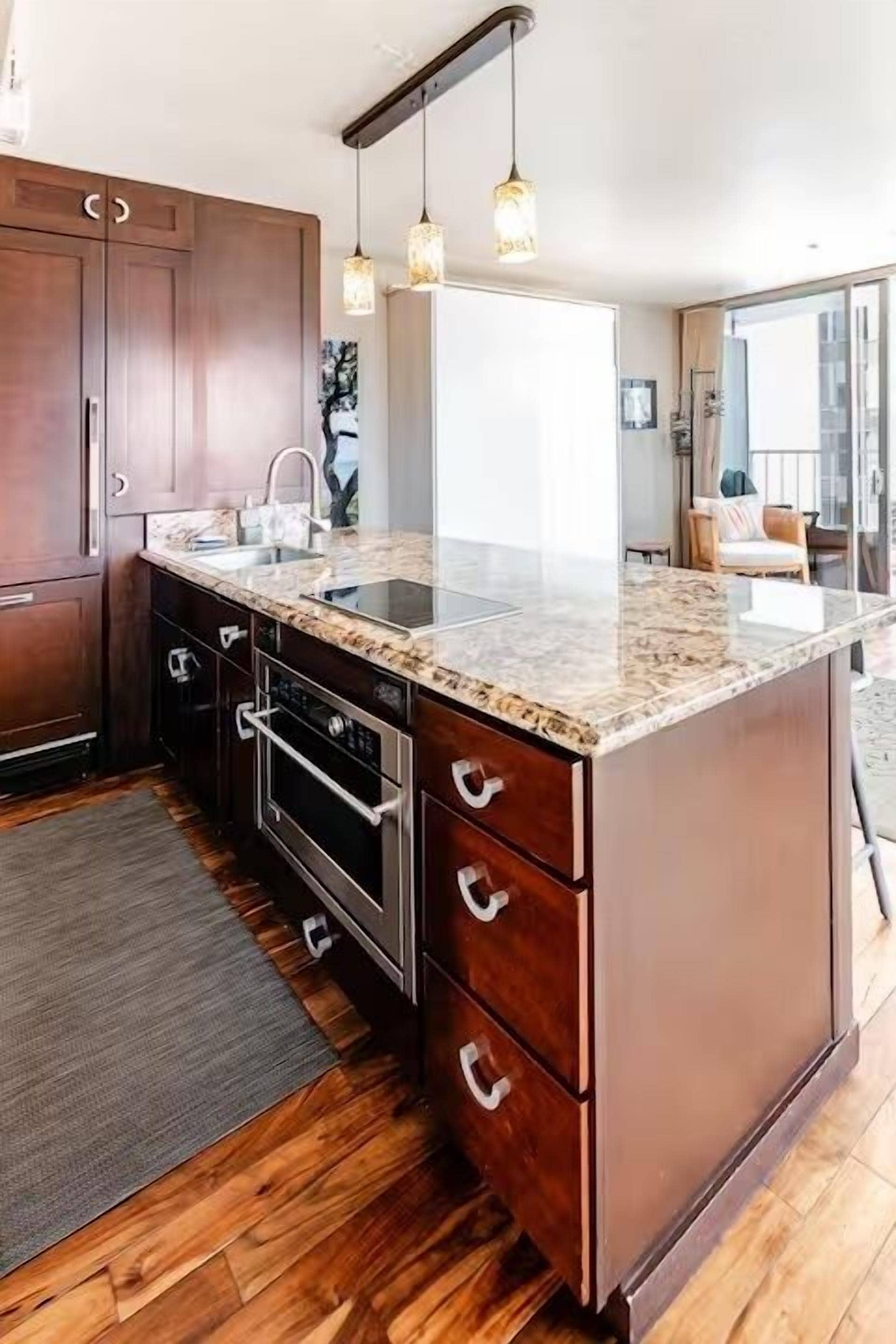 A kitchen with a granite countertop, wooden cabinets, a built-in oven, and pendant lighting.