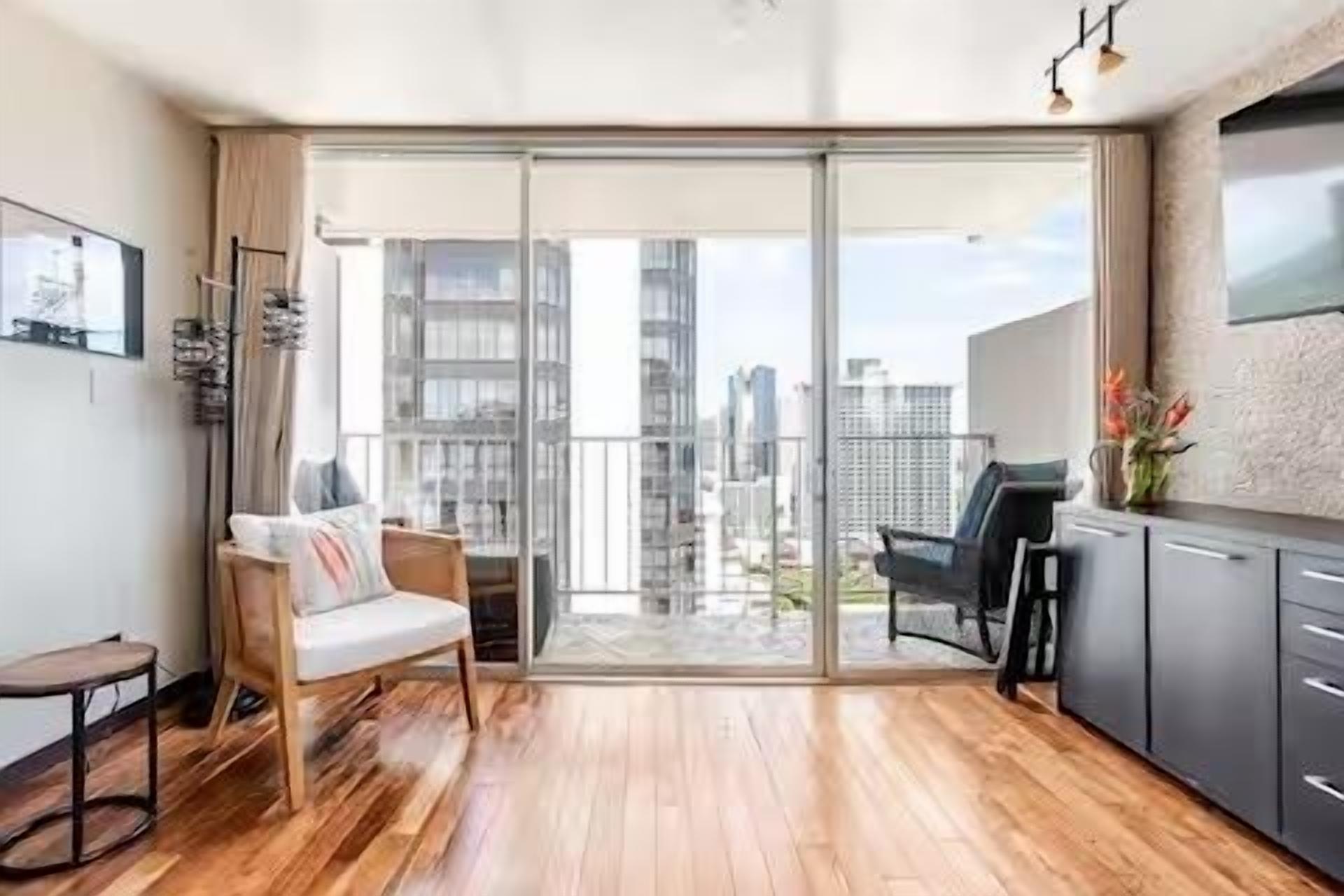A modern apartment with a balcony, wooden flooring, a sofa, a dining area, and a kitchen.
