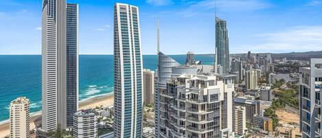 A coastal cityscape with high-rise buildings, including a prominent skyscraper with a unique design and a beach in the background.