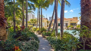 A pathway leading to a pool area surrounded by palm trees and tropical plants. - Chevron Renaissance River View (Surfers Paradise)