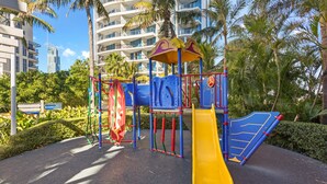 A playground with a yellow slide, blue climbing structures, and a red and yellow climbing wall. - Chevron Renaissance River View (Surfers Paradise)