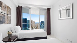 Ett modernt hotellrum med en stor säng, utsikt över staden och en silhuett av stadens byggnader som syns genom fönstret.