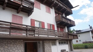 A two-story building with a stone facade, wooden balconies, and red shutters. - Faloria Mini (Cortina d´Ampezzo)