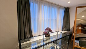 Habitación moderna con barandilla de vidrio, una planta en maceta y vistas al exterior a través de cortinas translúcidas.
