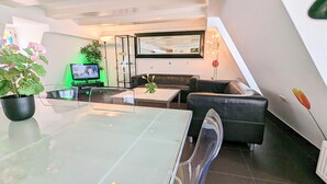 Un salón moderno con una mesa de comedor de cristal, sofá de cuero negro y televisor.