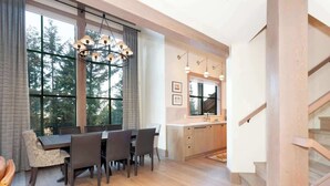 Een moderne eethoek met een groot raam, een kroonluchter en een keuken met aanrecht en spoelbak.