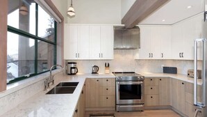 Een moderne keuken met witte kastjes, een roestvrijstalen fornuis en een groot raam.