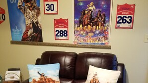 Een bruine leren bank met twee sierkussens, een poster van een rodeo en een lijst met een certificaat aan de muur.