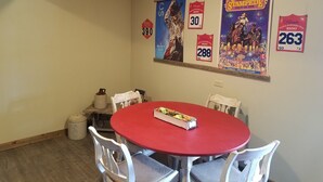 Een eetgedeelte met een rode tafel en witte stoelen, posters aan de muur en een prullenbak.