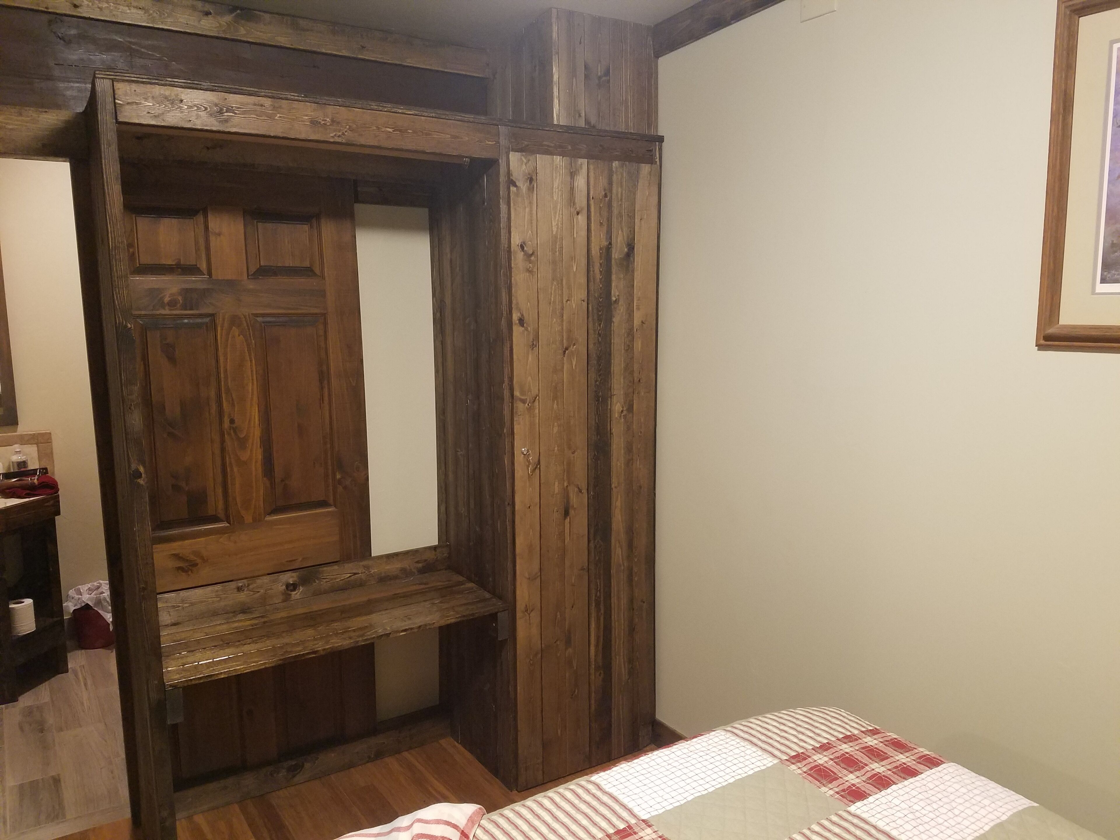 Une pièce avec une armoire en bois, un lit recouvert d’une couverture à carreaux et un tableau encadré accroché au mur.
