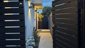 A narrow pathway leading to a modern house with a black gate, a small garden, and a water feature. - New Modern Beach Apartment (Carlsbad)