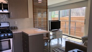 A modern kitchen with a built-in stove, a dining area with a TV, and a large sliding glass door to the outdoors. - New Modern Beach Apartment (Carlsbad)