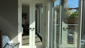 A modern hotel room with a large sliding glass door leading to a balcony, a bed with a striped cover, and a chair. - New Modern Beach Apartment (Carlsbad)