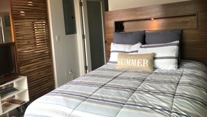 A bedroom with a bed, a wooden headboard, a television, and a sign above the door. - New Modern Beach Apartment (Carlsbad)