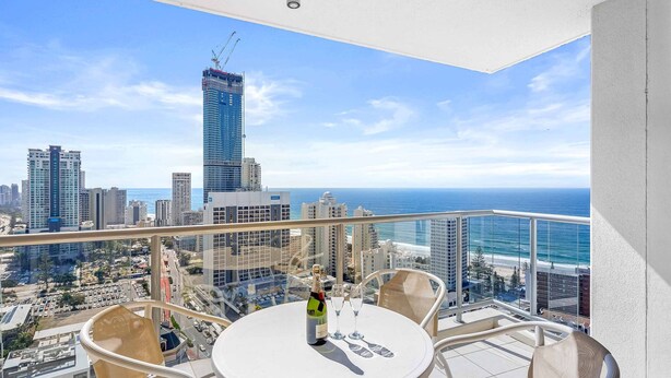 A balcony with a table, chairs, and a bottle of champagne. The balcony overlooks a cityscape with tall buildings and a view of the ocean. - Chevron Renaissance Ocean View (Surfers Paradise)