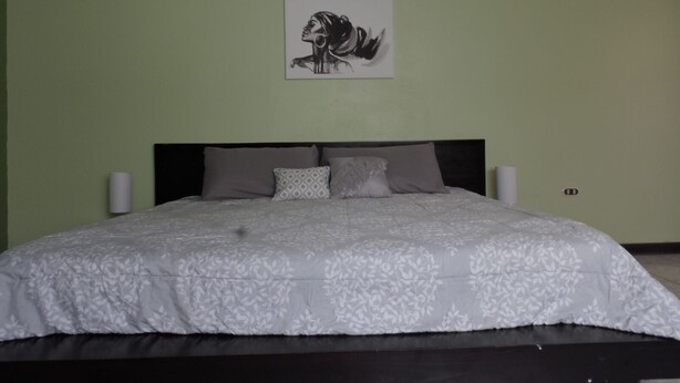 Een slaapkamer met een bed, een hoofdbord, twee wandlampen en een kunstwerk in een lijst erboven.