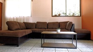 Een woonkamer met een hoekbank, een bijzettafeltje en een raam met gordijnen.