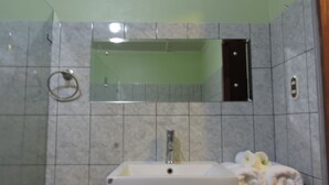 Een badkamer met een rechthoekig wastafelmeubel, een spiegel erboven en een handdoekrek aan de linkerkant.